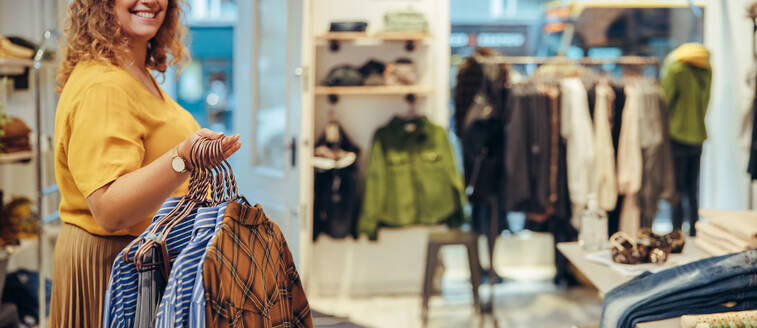 Cropped shot of a woman holding and moving clothes in her store. Fashion shop owner working in her store. - JLPSF08699