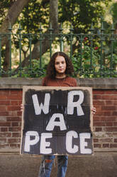 Junge Friedensaktivistin blickt in die Kamera und hält ein Antikriegsplakat in der Hand. Ein junges Mädchen protestiert gegen Krieg und Gewalt. - JLPSF08838