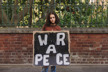Junger Friedensaktivist mit Antikriegsplakat in der Hand, der in die Kamera schaut. Teenager protestiert gegen Krieg und Gewalt. - JLPSF08839