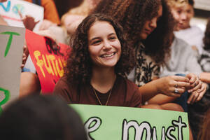 Fröhlich lächelndes Teenager-Mädchen, das in einer Gruppe von Klimaaktivisten sitzt. Multikulturelle Demonstranten, die für Klimagerechtigkeit und ökologische Nachhaltigkeit demonstrieren. - JLPSF08856