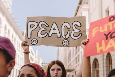 Group of teenagers marching the streets for world peace. Youth activists raising banners and placards during an anti-war rally in the city. Diverse young people protesting against war and violence. - JLPSF08859
