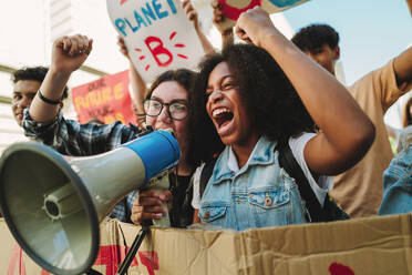 Youth climate activists shouting on a megaphone while marching against climate change. Young people protesting against global warming and pollution. Teenagers joining the global climate strike. - JLPSF08863