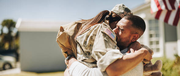 Eine Soldatin umarmt ihren Mann, nachdem sie von der Armee nach Hause zurückgekehrt ist. Eine amerikanische Soldatin erlebt ein emotionales Wiedersehen mit ihrem Mann, nachdem sie ihrem Land im Militär gedient hat. - JLPSF09067