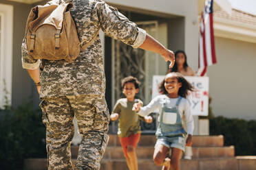 Aufgeregte Kinder, die ihren Vater umarmen. Militärischer Vater, der von seiner Frau und seinen Kindern zu Hause herzlich empfangen wird. Amerikanischer Soldat, der nach seinem Dienst in der Armee zu seiner Familie zurückkehrt. - JLPSF09100