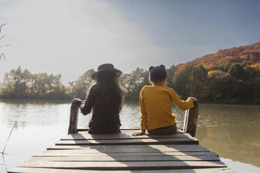 Boy and girl sitting on jetty at lake - OSF01067