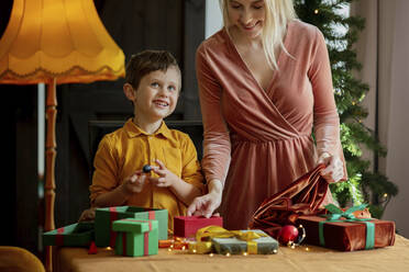 Glücklicher Junge mit Mutter beim Einpacken von Weihnachtsgeschenken auf dem Tisch zu Hause - VSNF00008