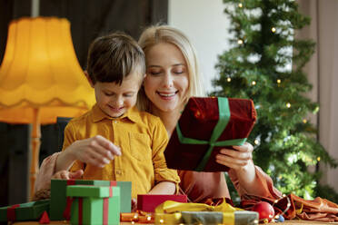 Mother and son wrapping Christmas gifts together at home - VSNF00009