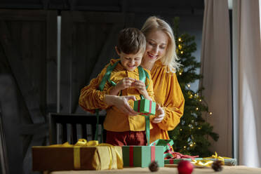 Junge hilft Mutter beim Einpacken von Weihnachtsgeschenken zu Hause - VSNF00015