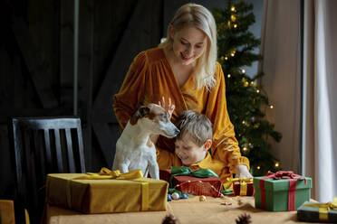 Mutter und Sohn mit Hund stehen neben eingepackten Geschenken auf dem Tisch zu Hause - VSNF00018