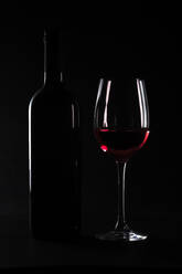 Dark studio shot of bottle and glass of red wine - JTF02238