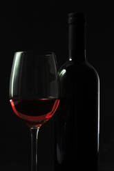 Dark studio shot of bottle and glass of red wine - JTF02239