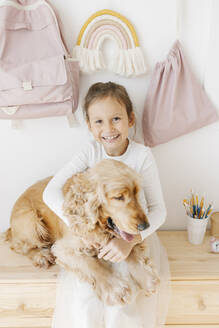 Glückliches Mädchen umarmt Hund sitzt auf Schrank - SSYF00019