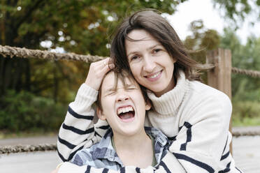 Lächelnde Mutter umarmt schreienden Sohn im Park - EYAF02180
