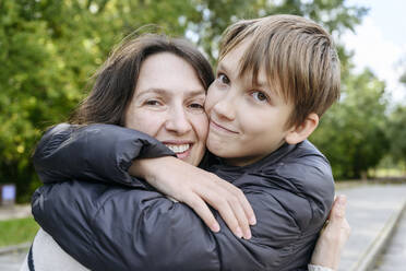 Lächelnde Mutter und Sohn umarmen sich im Park - EYAF02183