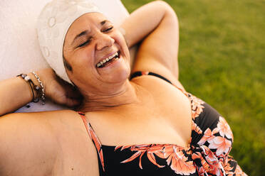 Ecstatic senior woman relaxing on a lounger in a swimsuit. Carefree elderly woman laughing cheerfully while vacationing at a luxury spa resort. Happy mature woman enjoying herself after retirement. - JLPSF09123