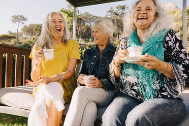 Ältere Frauen lachen fröhlich beim gemeinsamen Tee. Eine Gruppe älterer Freunde genießt ihren Sommerurlaub in einem Kurort. Drei reife Frauen, die sich nach ihrer Pensionierung amüsieren. - JLPSF09143