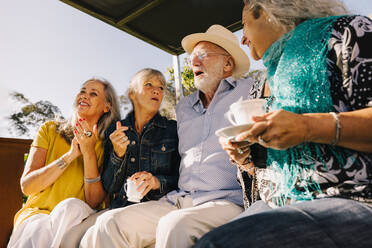 Alte Freunde lachen fröhlich beim gemeinsamen Tee. Fröhliche ältere Menschen, die ihren Sommerurlaub in einem Kurort genießen. Senioren, die nach ihrer Pensionierung gemeinsam Spaß haben. - JLPSF09145