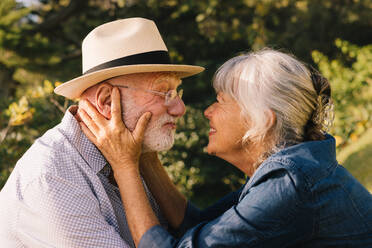 Grauhaariges Paar, das sich liebevoll anlächelt. Glückliches älteres Paar, das einen romantischen Moment in einem Park verbringt. Fröhliches älteres Paar, das sich im Freien anbetet. - JLPSF09150