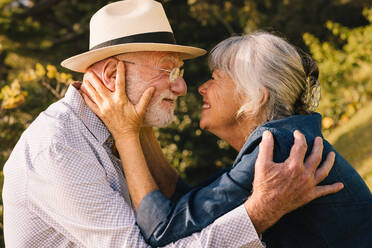 Happy senior couple smiling at each other with love and affection. Grey-haired couple sharing a romantic moment while standing in a park. Cheerful elderly couple adoring each other outdoors. - JLPSF09151