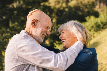 Glückliches älteres Paar, das sich liebevoll anlächelt. Fröhliches reifes Paar, das einen romantischen Moment miteinander teilt, während es in einem Park steht. Älteres Paar, das seine Liebe und Zuneigung im Freien ausdrückt. - JLPSF09155