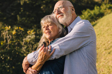 Romantisches älteres Paar, das sich im Park umarmt. Älteres Paar, das in den Armen des anderen die Sonne genießt. Älteres Paar, das nach dem Ruhestand Zeit miteinander verbringt. - JLPSF09161