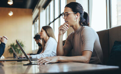 Junge Geschäftsfrau bei einem virtuellen Meeting in einem Co-Working Space. Geschäftsfrau hört während eines wichtigen Videogesprächs aufmerksam zu. Unternehmerin bei der Arbeit in einem modernen Arbeitsraum. - JLPSF09251