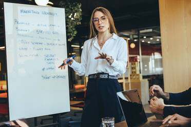Smart businesswoman discussing her marketing ideas with her team in a modern workspace. Confident young businesswoman giving a presentation during a meeting with her colleagues. - JLPSF09262