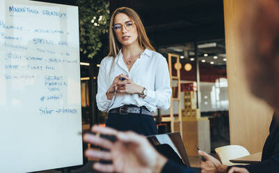 Young businesswoman discussing marketing ideas with her team in a modern workspace. Confident young business manager giving a presentation during a meeting with her colleagues. - JLPSF09263