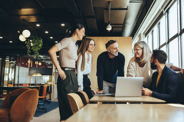 Smiling businesspeople having a discussion while collaborating on a new project in an office. Group of happy businesspeople using a laptop while working together in a modern workspace. - JLPSF09278