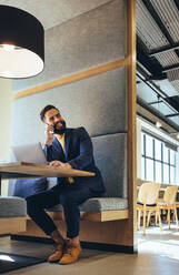 Young businessman speaking on a phone call. Happy young businessman smiling while communicating with his business partners. Successful entrepreneur working in a modern workspace. - JLPSF09314