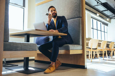 Business professional speaking on a phone call. Focused young businessman communicating with his business partners over the phone. Young entrepreneur working in a modern workspace. - JLPSF09317