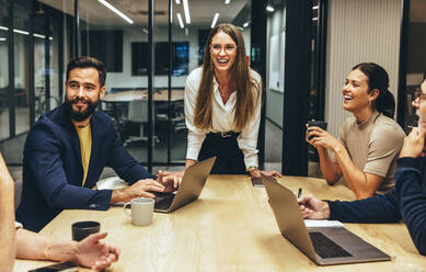 Fröhliche Geschäftsleute, die während einer Sitzung in einem Sitzungssaal lachen. Ein Team erfolgreicher Geschäftsleute, die die Zusammenarbeit an einem modernen Arbeitsplatz genießen. Fröhliche Geschäftsleute, die zusammenarbeiten. - JLPSF09346