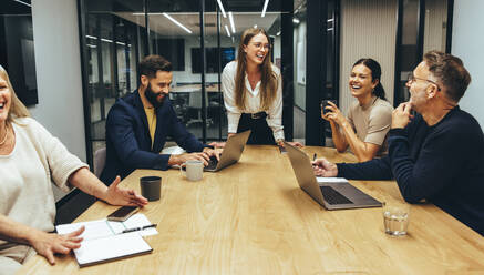 Fröhlich lachende Kollegen während einer Sitzung in einem Sitzungssaal. Eine Gruppe glücklicher Geschäftsleute, die die Zusammenarbeit an einem modernen Arbeitsplatz genießen. Erfolgreiche Geschäftsleute, die zusammenarbeiten. - JLPSF09347