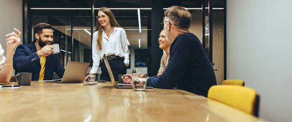 Erfolgreiche Geschäftsleute bei einer Besprechung in einem Sitzungssaal. Eine Gruppe glücklicher Geschäftsleute lächelt fröhlich, während sie in einem Büro zusammenarbeiten. Ein Team aus verschiedenen Kollegen arbeitet zusammen. - JLPSF09348