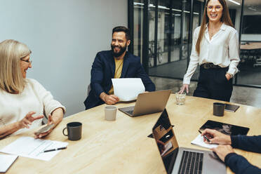 Business professionals laughing during a meeting in a boardroom. Group of successful businesspeople enjoying working together in a modern workplace. Happy colleagues collaborating on a new project. - JLPSF09349