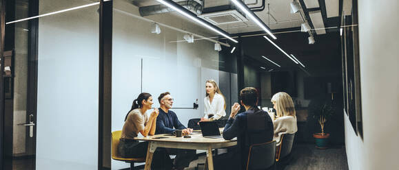 Eine Gruppe von Kollegen, die in einem transparenten Sitzungssaal eine Besprechung abhalten. Ein Team aus verschiedenen Geschäftsleuten, die während eines Briefings eine Diskussion führen. Geschäftsleute, die an einem neuen Projekt zusammenarbeiten. - JLPSF09352