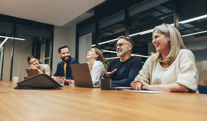 Fröhliche Geschäftsleute, die während einer Sitzung in einem Sitzungssaal lachen. Ein Team aus verschiedenen Geschäftsleuten, die an einem modernen Arbeitsplatz zusammenarbeiten. Kollegen, die an einem neuen Projekt arbeiten. - JLPSF09353