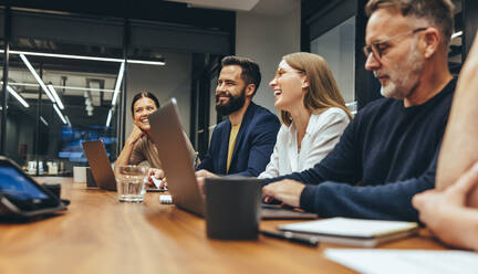 Positive businesspeople having a meeting in a boardroom. Group of happy businesspeople smiling while working together in a modern workplace. Diverse business colleagues collaborating on a project. - JLPSF09356