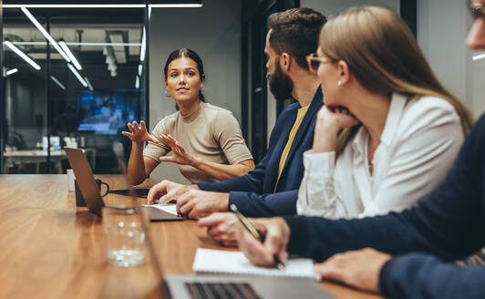 Junge Geschäftsfrau, die während einer Sitzung mit ihren Kollegen eine Diskussion führt. Gruppe von Geschäftsleuten, die an einem modernen Arbeitsplatz zusammenarbeiten. Geschäftskollegen, die an einem Projekt arbeiten. - JLPSF09358