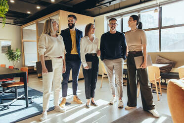 Eine Gruppe glücklicher Kollegen, die fröhlich lächelnd in einem Büro stehen. Ein Team erfolgreicher Geschäftsleute steht in einem kreativen und modernen Arbeitsplatz zusammen. - JLPSF09363