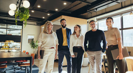 Erfolgreiche Geschäftsleute stehen zusammen in einem Büro. Ein Team von glücklichen Geschäftsleuten lächelt fröhlich, während sie in einem kreativen und modernen Arbeitsplatz stehen. - JLPSF09364