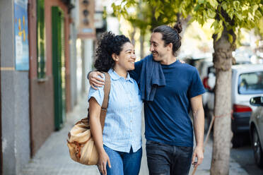 Smiling couple looking at each other and walking on footpath - JOSEF14471