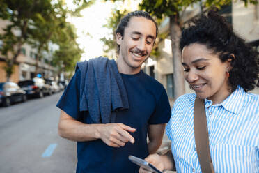 Lächelndes Paar teilt sich ein Smartphone auf der Straße - JOSEF14487