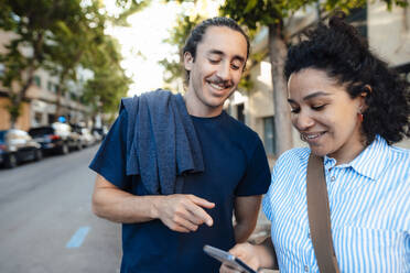 Smiling couple sharing smart phone on street - JOSEF14487