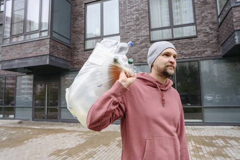 Mann trägt Müllsack auf der Schulter vor einem Gebäude - EYAF02193