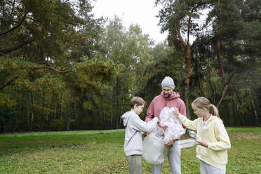 Man with son and daughter collecting garbage from grass - EYAF02203