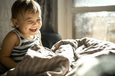 Süßes Baby lachend in Bettdecke auf Bett zu Hause - ANAF00183