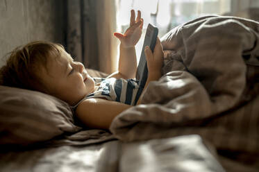 Ein kleiner Junge benutzt ein Mobiltelefon im Bett zu Hause - ANAF00184