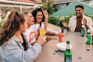 Ein kühles Bier und eine gute Zeit. Eine Gruppe fröhlicher junger Leute, die zusammen lachen, während sie auf einer Dachterrasse abhängen. Fröhliche Freunde, die am Wochenende alkoholische Getränke genießen. - JLPSF09370