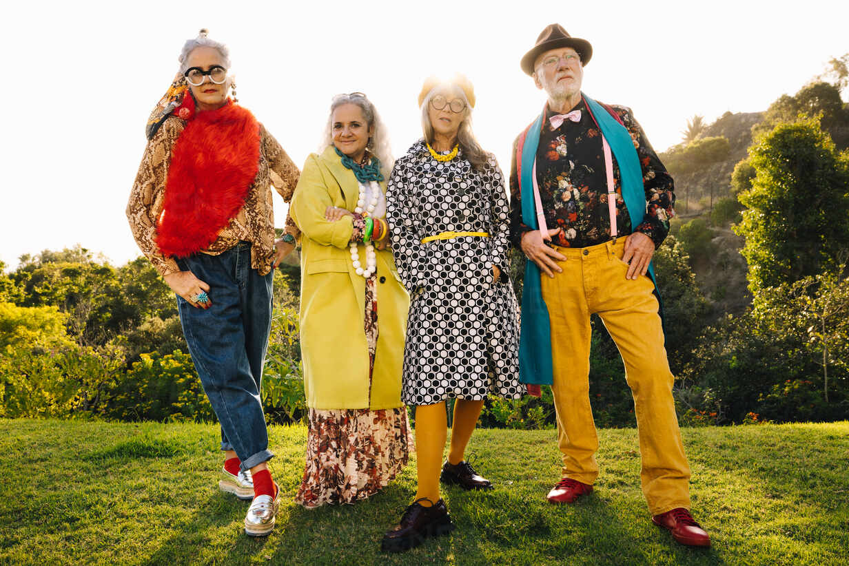 Four confident senior friends standing in a park on a sunny day. Group of  stylish elderly people wearing colourful casual clothing. Carefree senior  citizens enjoying their golden years. stock photo